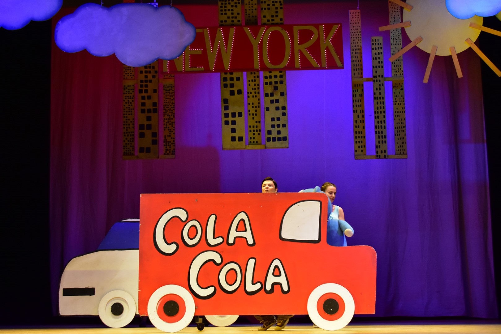 Na środku zdjęcia znajduje się białe auto z kartonu, wyprzedzane przez czerwoną furgonetkę coca-coli.